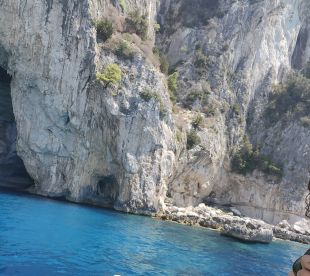 A scenic view of rocky cliffs and clear blue waters, possibly near a fishing location, with a person partially visible in the foreground.