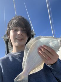 A young angler proudly displaying a freshly caught Flounder while on a fishing trip, with a clear blue sky in the background.