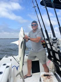 An angler proudly displaying a large shark while aboard a fishing boat, showcasing a successful day on the water.