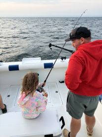 A young angler is focused on reeling in a fish while fishing on a boat, with a calm sea in the background.