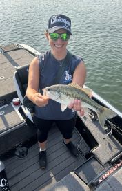Angler proudly displaying a large Largemouth Bass while standing on a fishing boat, showcasing a sunny day on the water.