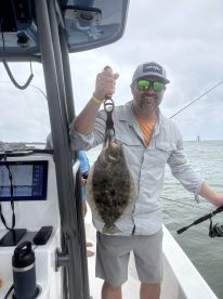 An angler proudly displaying a Flounder while fishing on a boat, showcasing the excitement of a successful catch.
