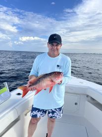 Angler holding a vibrant Red Snapper aboard a boat during a fishing trip in open waters.