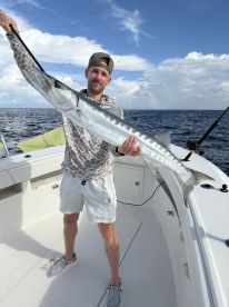 Angler proudly displaying a large Barracuda on a fishing charter in open waters, showcasing a successful day on the boat.