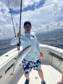 An angler proudly displaying a large King Mackerel while fishing on a boat in open waters.