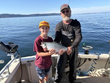 A young angler and an adult proudly displaying a freshly caught Salmon on a fishing boat, enjoying a sunny day on the water.