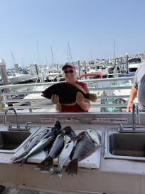 An angler proudly displaying a large Flounder at the cleaning station, surrounded by a variety of freshly caught fish after a successful day on the water.