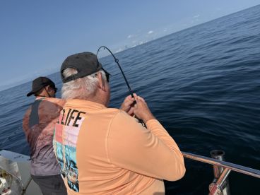 Two anglers engaged in fishing on a calm day at sea, showcasing the excitement of reeling in a catch.