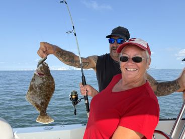 Two anglers celebrating a successful catch of a Flounder while fishing on a sunny day.