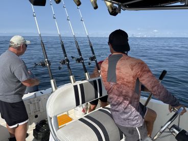 Two anglers actively fishing on a boat, with multiple fishing rods set up for a day on the water.