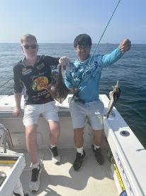 Two anglers proudly displaying their catch, including a large fish, while fishing on a boat in open waters.