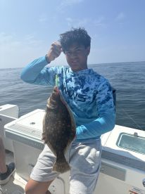 A young angler proudly displaying a Flounder while fishing on a boat, showcasing a successful catch during a sunny day on the water.