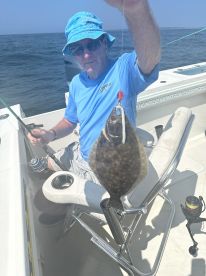 An angler proudly displaying a caught Flounder while seated on a boat, enjoying a day of fishing in open waters.