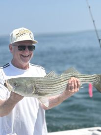 An angler proudly displaying a large striped bass while fishing on a sunny day.