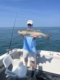 An angler proudly displaying a large Striped Bass while fishing on a sunny day.