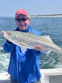 An angler proudly displaying a large Striped Bass while out on the water, showcasing a successful fishing trip.