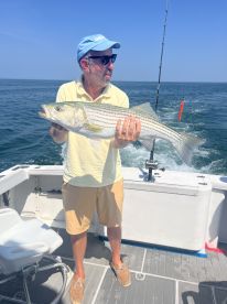 An angler proudly displaying a large Striped Bass while fishing on a boat in open waters.