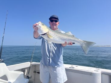Angler proudly displaying a large Striped Bass while aboard a fishing boat in clear waters.