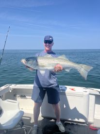 An angler proudly displaying a large Striped Bass while fishing on a boat in open waters.