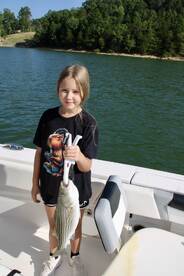 A young angler proudly displaying a striped bass while fishing on a scenic lake.