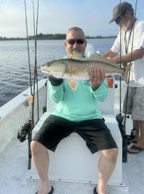 An angler proudly displays a large Redfish while seated on a boat, showcasing a successful day of fishing.