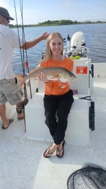 A young angler proudly displaying a Redfish while seated on a boat during a fishing trip.