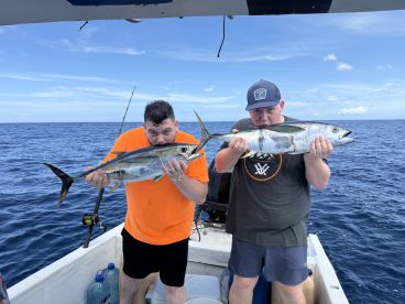 Two anglers proudly displaying their catches of Amberjack while fishing offshore, showcasing a beautiful day on the water.