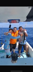 Three anglers celebrating their catch aboard a fishing boat in open water, showcasing a large fish.