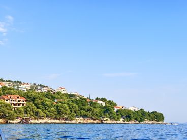 A scenic view of a coastal village from the water, showcasing lush greenery and residential buildings along the shoreline.