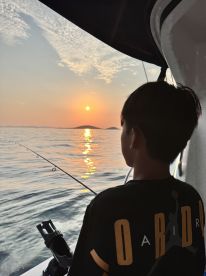 A young angler fishing at sunset, enjoying a serene moment on the water with a beautiful reflection of the sun.