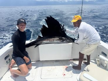 A young angler and a guide proudly display a large Sailfish on a sport fishing boat, showcasing a successful deep-sea fishing trip.