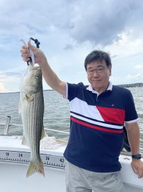 An angler proudly displaying a large Striped Bass while fishing on a boat, showcasing a successful day on the water.