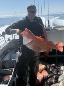 An angler proudly displaying a large Orange Rockfish on a fishing charter in open waters.