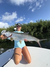 Angler proudly displaying a large Tarpon while fishing in a mangrove area, showcasing a successful day on the water.