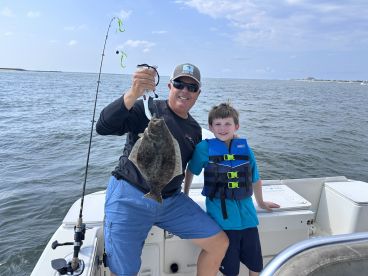 A proud angler and a young boy display a Flounder while fishing on a boat, showcasing a memorable moment on the water.