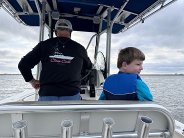 A young boy in a blue life jacket sits on the boat, while the captain navigates the waters, showcasing a relaxed fishing environment.