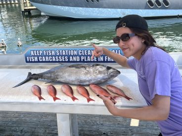 An angler proudly displays a large Blackfin Tuna alongside several smaller Red Snapper at a fish cleaning station, showcasing a successful day of fishing.