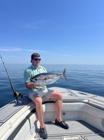 An angler proudly displaying a large Tuna while seated on a boat in calm waters, showcasing a successful fishing trip.