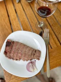 A plate of sliced meat accompanied by red onions and a glass of red wine, set on a wooden table.