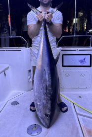 Angler proudly displaying a large Bluefin Tuna on the deck of a fishing boat, showcasing a successful night fishing trip.