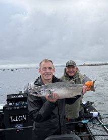 Two anglers proudly displaying a large Chinook Salmon aboard a fishing boat, showcasing a successful day on the water.