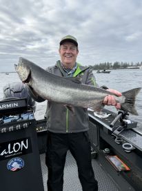 An angler proudly displaying a large Salmon while fishing from a boat in a scenic waterway.