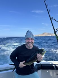 Angler proudly displaying a Mahi Mahi while fishing off the coast, with a scenic backdrop of the ocean and land.