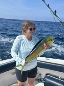 A smiling angler holding a vibrant Mahi Mahi while fishing offshore, showcasing a successful catch during a sunny day on the water.