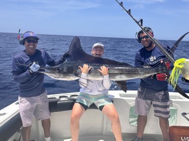 Three anglers proudly displaying a large Sailfish on a sport fishing boat, showcasing a successful deep-sea fishing trip.