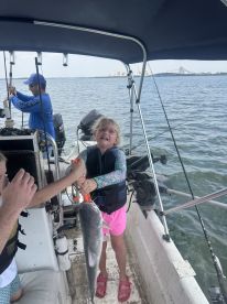A young girl proudly displaying a caught fish while on a boat, enjoying a family fishing trip.
