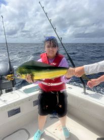 A young angler proudly displaying a vibrant Mahi Mahi while fishing on a boat in open waters.