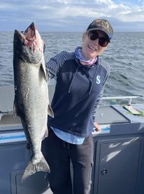 An excited angler proudly displaying a large Salmon on a fishing boat, showcasing a successful day on the water.
