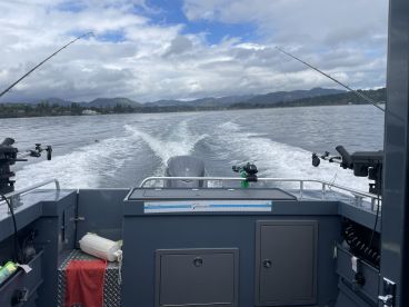 View from the helm of a modern fishing boat cruising through calm waters, showcasing the scenic backdrop of mountains and shoreline.