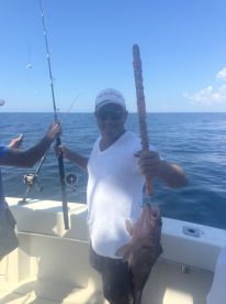 An angler proudly displaying a large Grouper caught while fishing on a boat in clear blue waters.